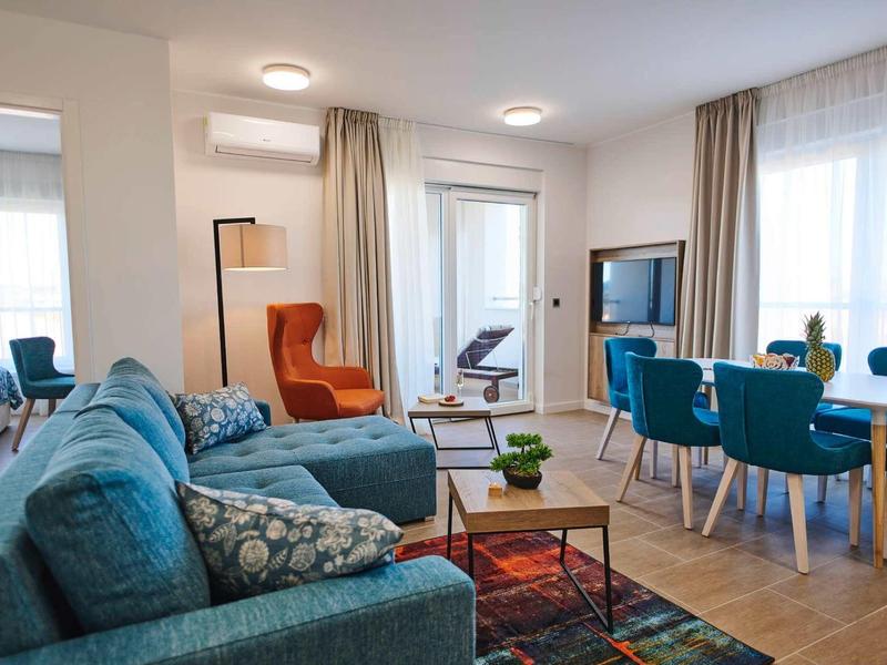 Modern woonkamer met blauwe bank, eettafel en toegang tot balkon.