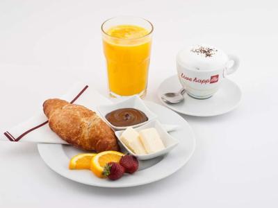 Frühstück mit Croissant, Schokolade, Butter, Früchten, Orangensaft und Kaffee in weißem Geschirr.