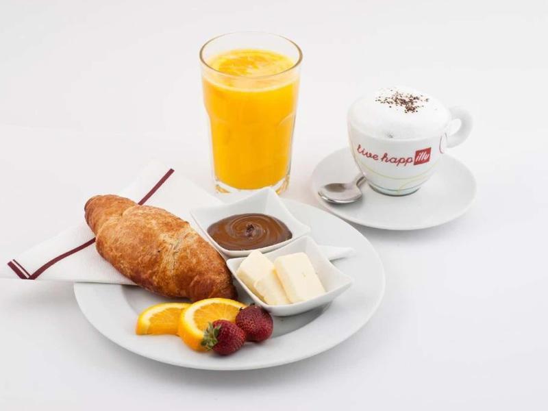 Frühstück mit Croissant, Schokolade, Butter, Früchten, Orangensaft und Kaffee in weißem Geschirr.