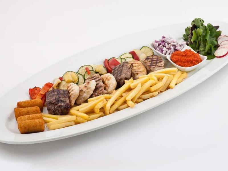 Großer Teller mit Pommes, Steak, Hähnchen, Gemüse, Soßen und Kroketten, bunt und appetitlich.