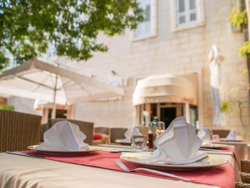 Restauranttisch im Freien mit weißem Geschirr, Stoffservietten und Sonnenschirm bei Tageslicht.