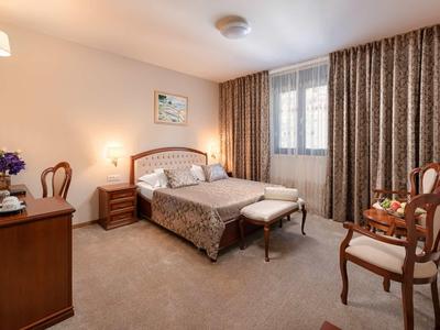 Przytulny pokój hotelowy z podwójnym łóżkiem, krzesłami, zasłonami i ciepłym oświetleniem.