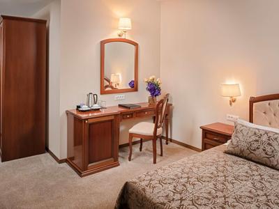 Pokój hotelowy z biurkiem, krzesłem, łóżkiem i szafą w ciepłych odcieniach drewna