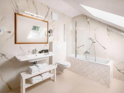 Jasna łazienka z marmurowymi płytkami, wanną i umywalką pod oknem dachowym.