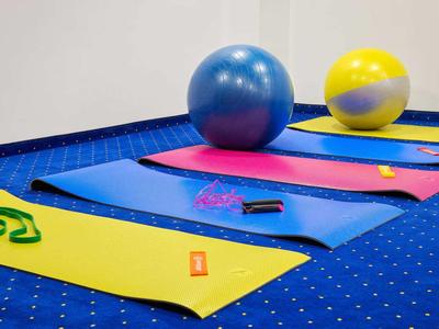 Bunte Yogamatten und Fitnessbälle auf blauem Teppich in einem Übungsraum.
