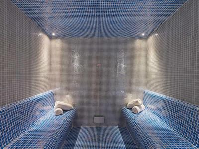 Luksusowa łaźnia parowa z niebieskimi kafelkami i zwiniętymi ręcznikami na ławkach.