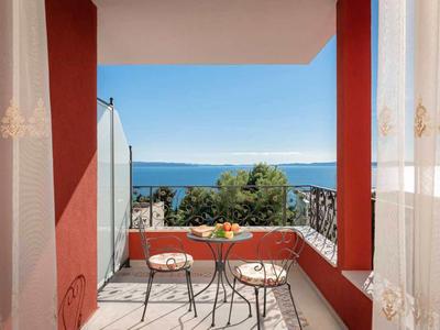 Balkon z małym stolikiem i dwoma krzesłami, widok na morze i czyste niebo.