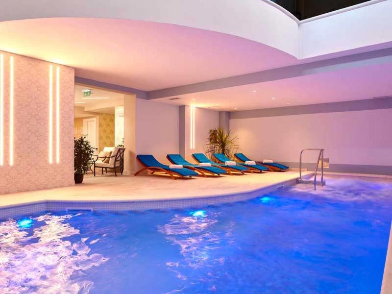 Basen kryty z niebieskim oświetleniem i leżakami w nowoczesnej strefie spa.