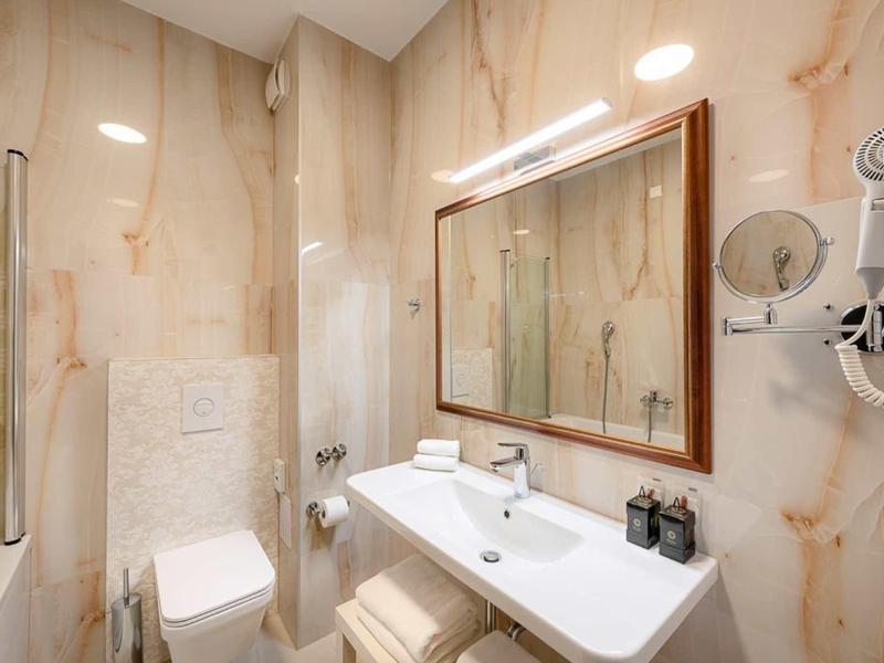 Kompaktowa łazienka z umywalką, lustrem i toaletą, płytki w jasnobrązowy wzór marmuru