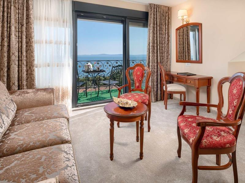 Przytulny salon z częścią wypoczynkową i balkonem z widokiem na morze w pokoju hotelowym.