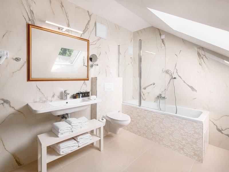 Jasna łazienka z marmurowymi płytkami, wanną i umywalką pod oknem dachowym.