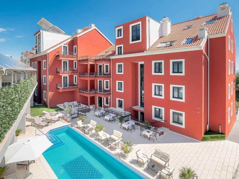 Nowoczesny czerwony budynek hotelu z basenem i tarasem pod niebieskim niebem.