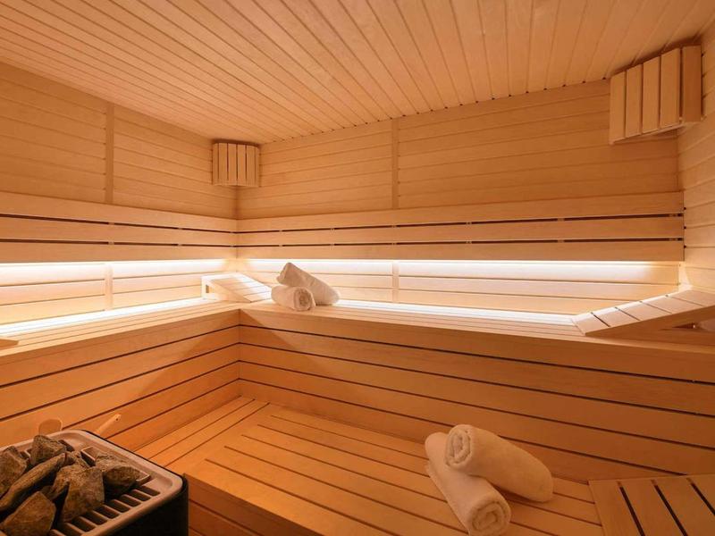 Jasna drewniana sauna z ławkami, ręcznikami i piecem do sauny w dolnym lewym rogu.