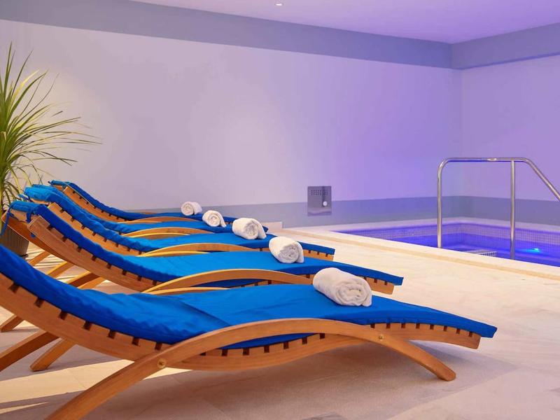 Kilka niebieskich leżaków z białymi ręcznikami obok krytego basenu w hotelu.