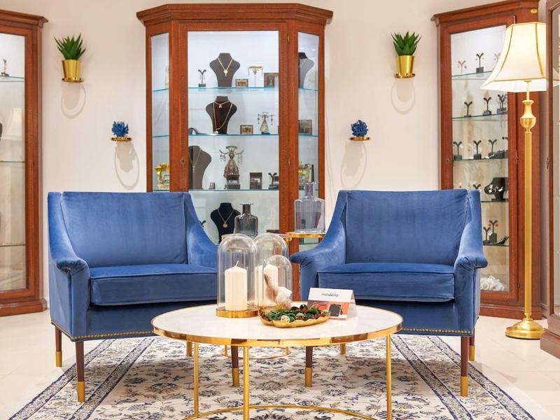 Przytulny kącik z dwoma niebieskimi fotelami i okrągłym stołem przed gablotami z dekoracjami.