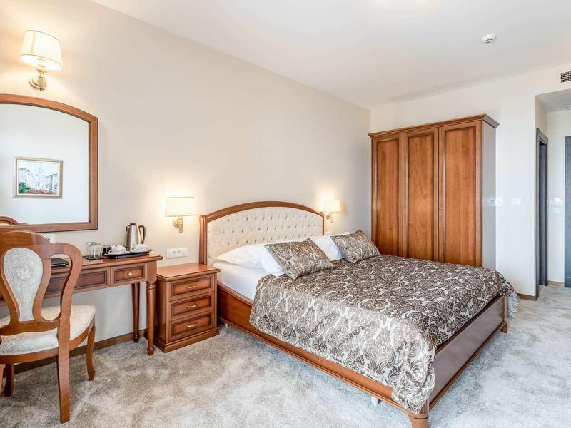 Jasny pokój hotelowy z podwójnym łóżkiem, drewnianymi meblami, biurkiem i wykładziną.