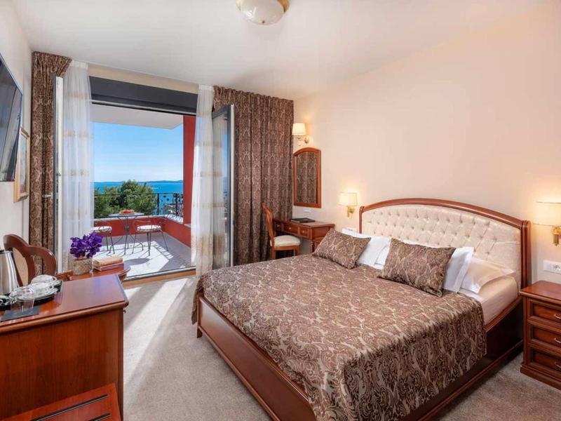 Sypialnia z podwójnym łóżkiem, telewizorem, biurkiem i balkonem z widokiem na morze.