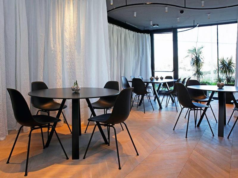 Moderner Essbereich mit runden schwarzen Tischen, schwarzen Stühlen und großen Fenstern für viel Licht.