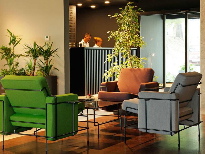 Moderner Wohnraum mit bunten Sesseln, Glas-Couchtisch und grünem Pflanzenarrangement.