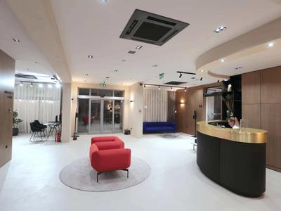 Moderna hall d'hotel con poltrona rossa, reception e pavimenti chiari.