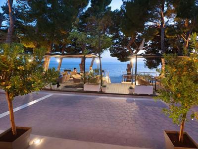 Vista di una terrazza con alberi, aree salotto e mare sullo sfondo al crepuscolo.