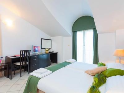 Modern hotel room with double bed, desk, and large window with green curtain.