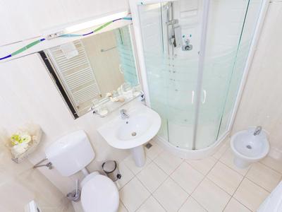 Compact white-tiled bathroom with shower, sink, toilet, and bidet.