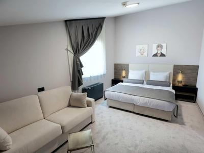 Modern hotel room with double bed, sofa, and large windows with curtains.