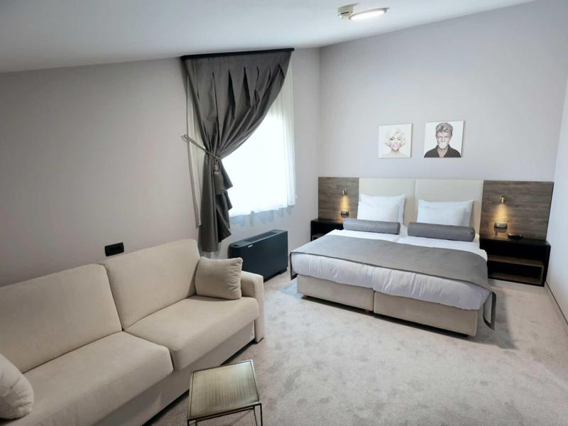 Modern hotel room with double bed, sofa, and large windows with curtains.