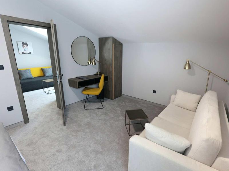 Modern hotel room with sofa, desk, and yellow chair.
