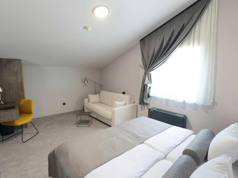 Bright hotel room with comfortable bed, sofa, and large window with curtains.