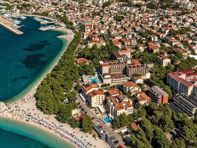 Veduta aerea di una città balneare con hotel, alberi verdi e una spiaggia sabbiosa affollata sul mare.