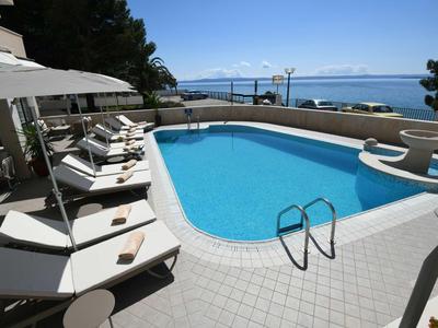 Pool area with sun loungers and umbrellas by the sea with mountain views.