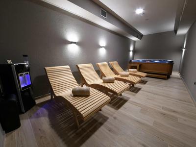 Area relax moderna con quattro lettini in legno, asciugamani e vasca idromassaggio con luce soffusa.