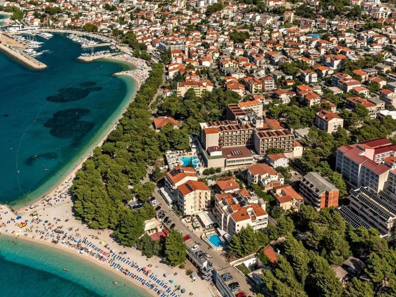 Veduta aerea di una città balneare con hotel, alberi verdi e una spiaggia sabbiosa affollata sul mare.
