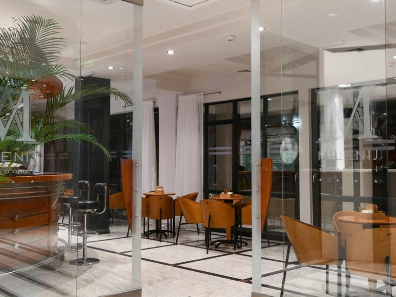 Area lounge di un hotel moderno con pareti di vetro, poltrone e mobili in legno su pavimento chiaro in marmo.