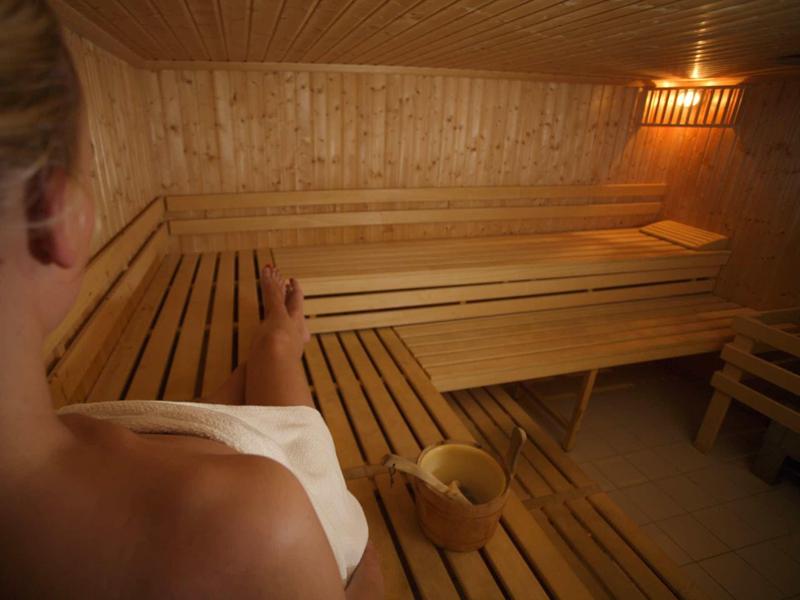 Persona rilassata in una sauna con panche di legno e mestolo per acqua.