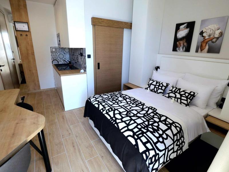 Camera d'hotel moderna con letto matrimoniale, dettagli in legno e angolo cottura sullo sfondo.