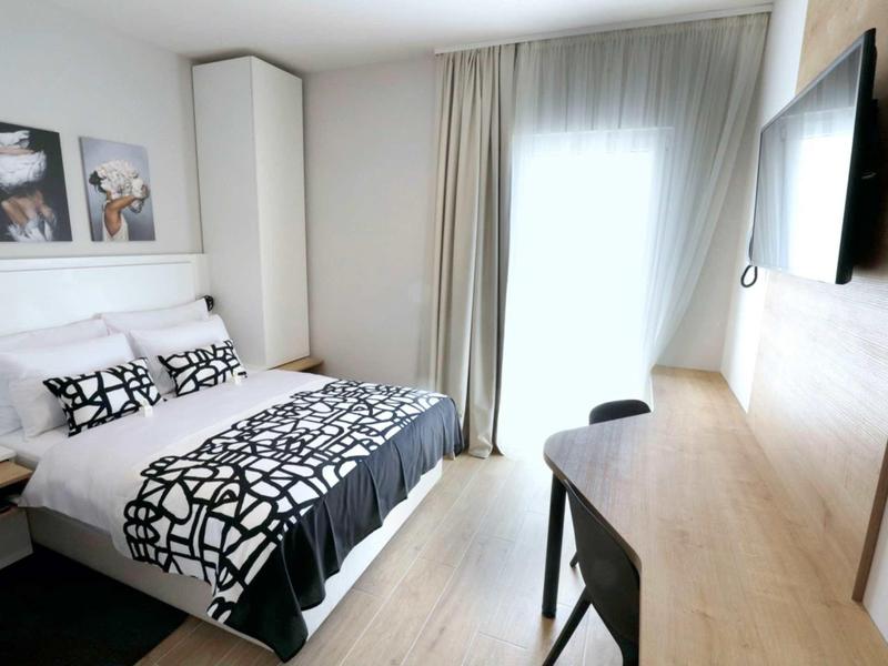 Camera d'albergo moderna con letto matrimoniale, scrivania e ampia finestra con tende.