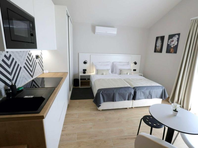 Camera d'hotel moderna con letto matrimoniale, angolo cottura e piccolo angolo pranzo con tavolo rotondo.