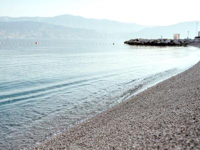 Playa de guijarros con agua tranquila y colinas en el horizonte bajo un cielo despejado.
