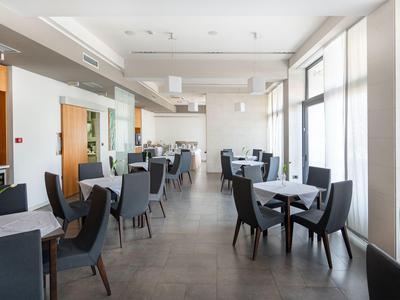 Comedor luminoso con varias mesas y sillas negras, grandes ventanales dejan entrar mucha luz.