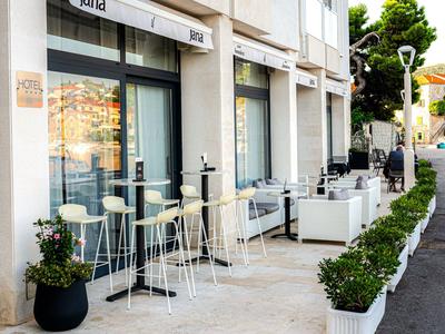 Área exterior moderna de hotel con taburetes de bar y asientos blancos junto a una acera.