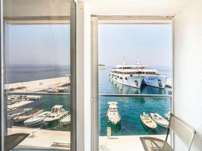 Vista a través de puertas de balcón abiertas hacia un puerto con barcos y un gran crucero en un día despejado.