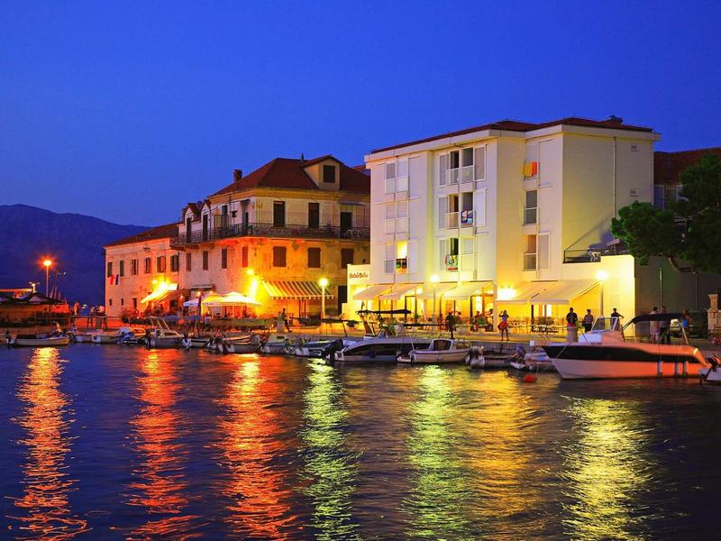 Hotel sul lungomare di notte con acqua illuminata e barche.