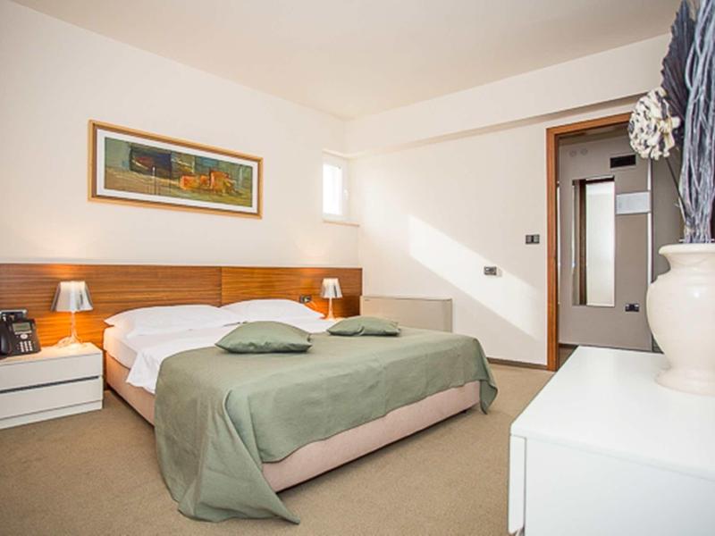 Camera d'hotel moderna con letto matrimoniale, coperta verde e comodini con lampade.