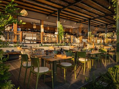 Espace extérieur ouvert d'un restaurant avec tables dressées et chaises vertes.