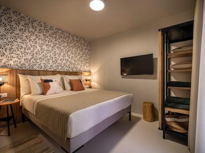 Cozy hotel room with double bed, TV, and open shelving unit with fresh towels.