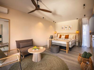 Bright hotel room with double bed, seating area, ceiling fan, and wooden floor.