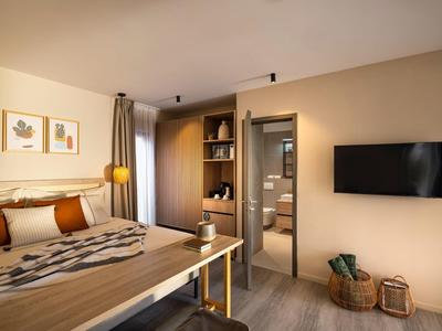 Modern hotel room with wooden furniture, bed, TV, and access to bathroom.